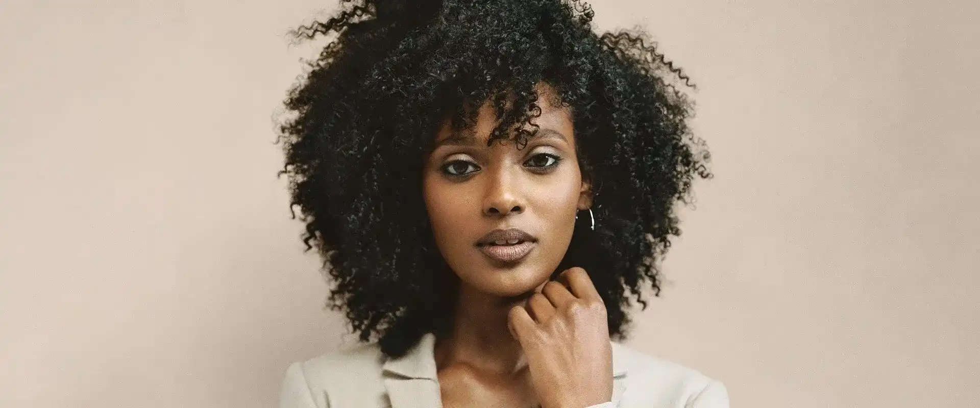 Young woman with curly hair in a thoughtful pose against a neutral background.