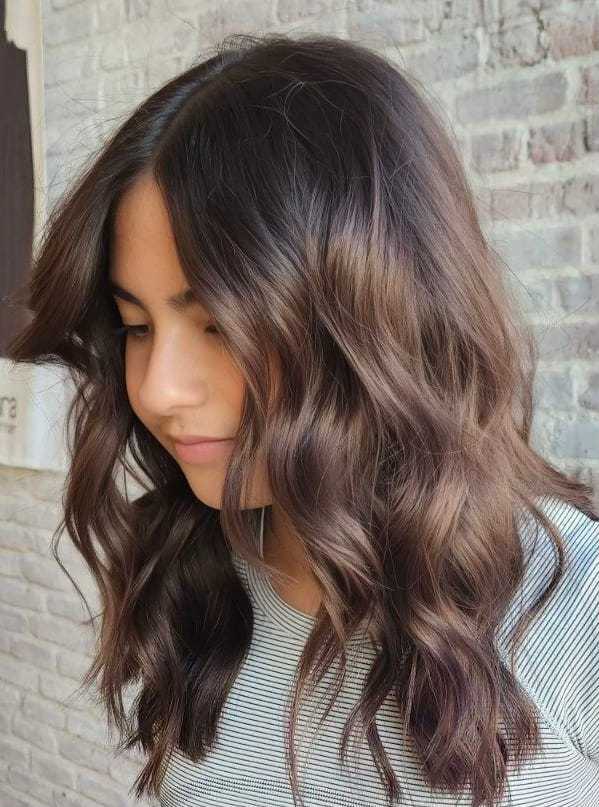 Woman with wavy brown hair and a striped shirt against a brick wall background.